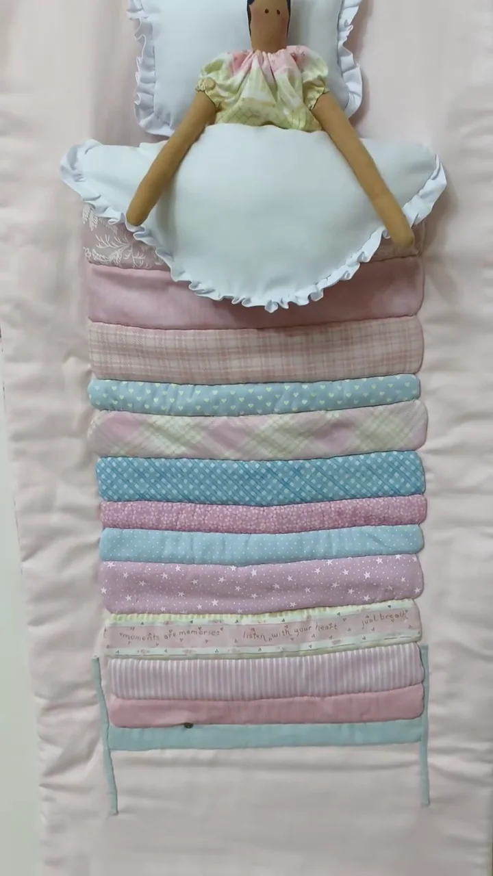Boneca Tilda sobre uma pilha de pequenos colchões em tecidos claros.