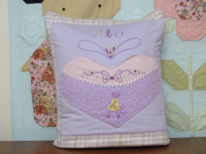 Almofada lilás com uma roupa de bailarina aplicada em tecido rosa e lilás.