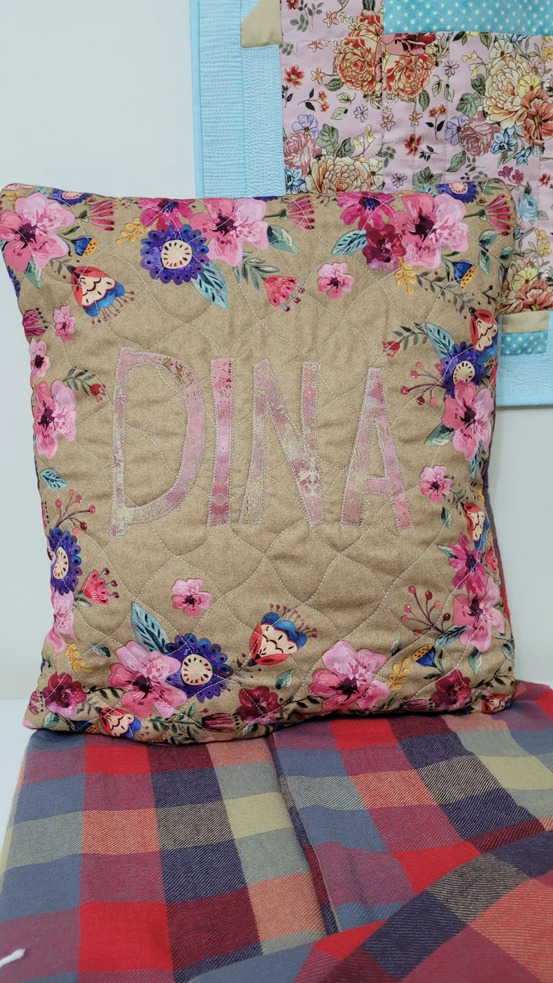 Almofada com flores rosa, monograma central e costuras de quilting.