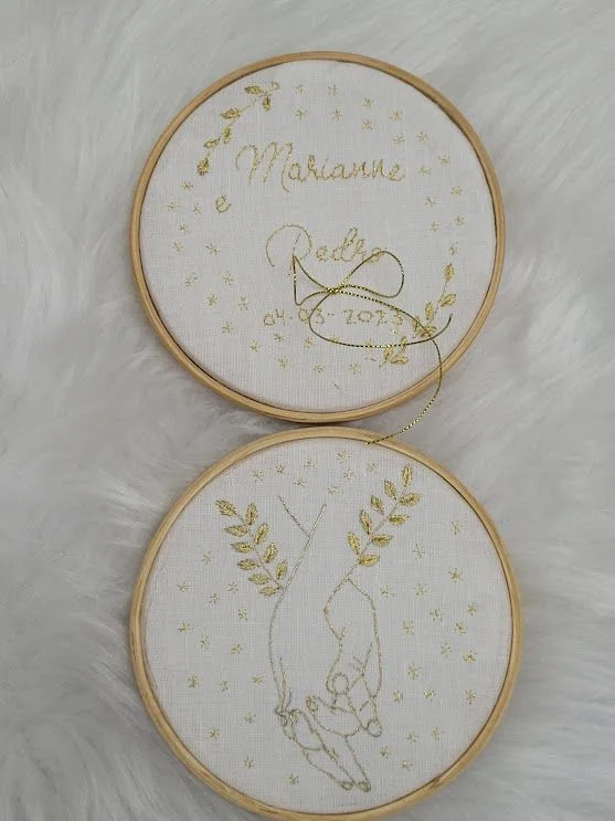 Dois bastidores claros bordados com nomes, ramos e pequenos desenhos.