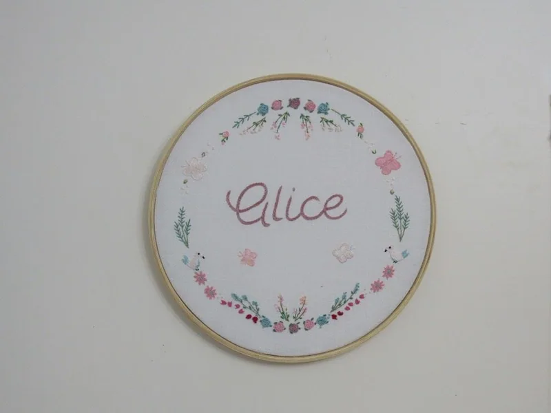 Bastidor com o nome Alice cercado de flores e folhas bordadas.