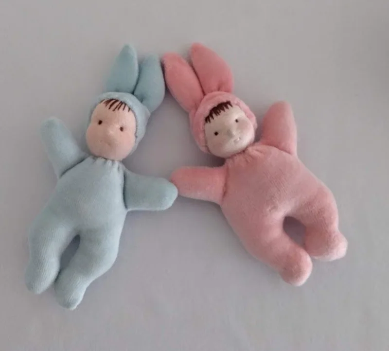 Dois pequenos bonecos com macacões rosa e azul e gorros com orelhas.