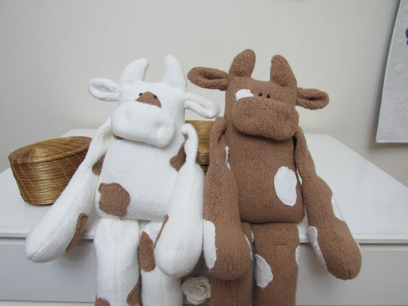 Dois bichos de tecido, um branco com manchas marrons e outro marrom com manchas brancas.