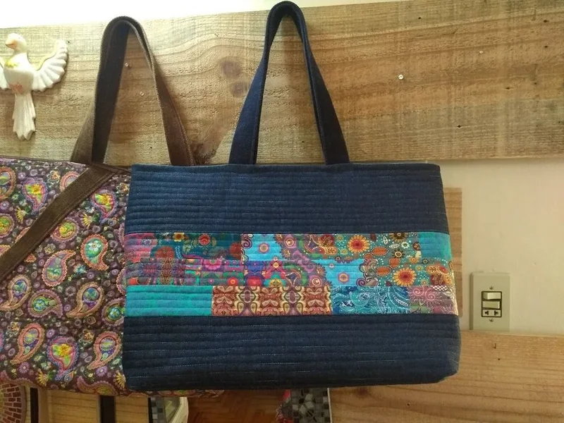 Bolsa azul-escura com faixa de pequenos retalhos coloridos e alças compridas.