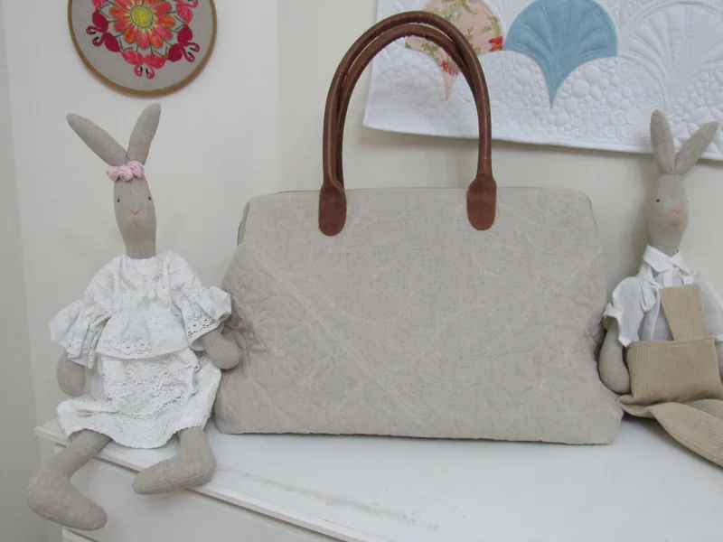 Bolsa clara com alças marrons, acompanhada de uma coelha de tecido.