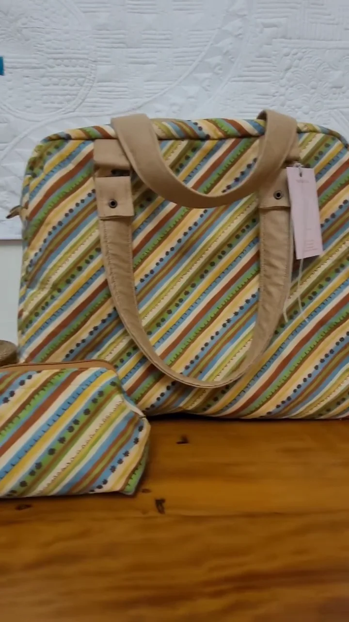 Bolsa de viagem listrada em azul, amarelo e branco ao lado de uma nécessaire do mesmo tecido.