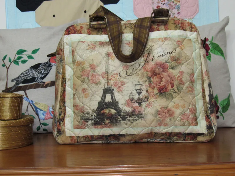 Bolsa com alças marrons, flores e desenhos da Torre Eiffel sobre fundo claro.