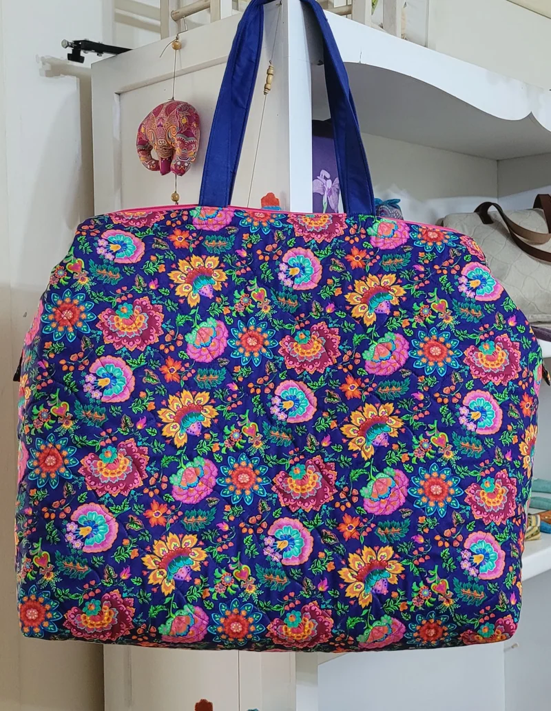 Bolsa de flores coloridas sobre fundo azul-escuro e alças azuis, pendurada em uma prateleira.
