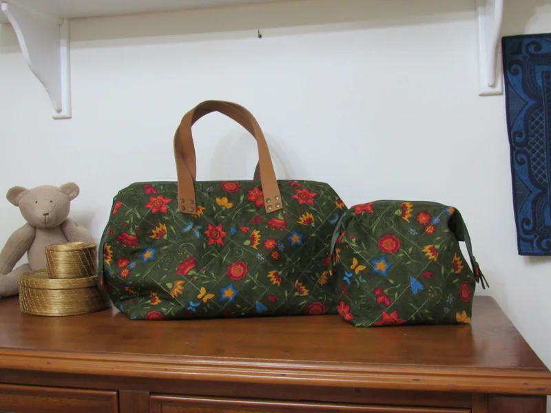 Bolsa verde de estampa floral e alças caramelo, sobre uma cômoda.