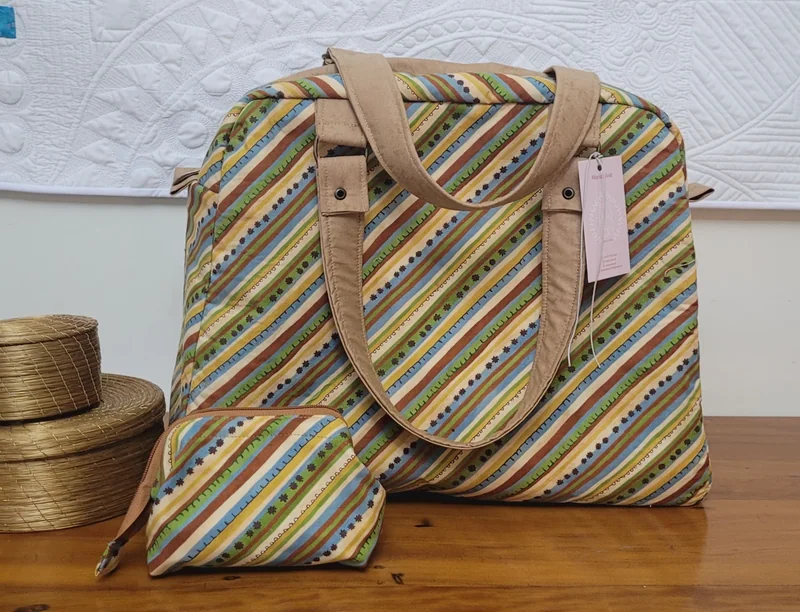 Bolsa de listras diagonais em verde, marrom e azul, com alças de mão e uma nécessaire pequena do mesmo tecido.