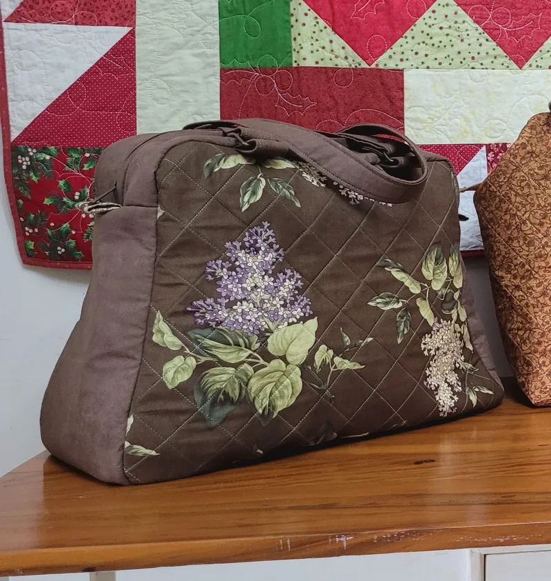 Bolsa marrom com quilting e ramo de lilases aplicado na frente, com alças curtas.