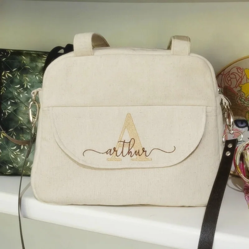 Bolsa de maternidade clara com alças e o nome Arthur bordado no bolso da frente.
