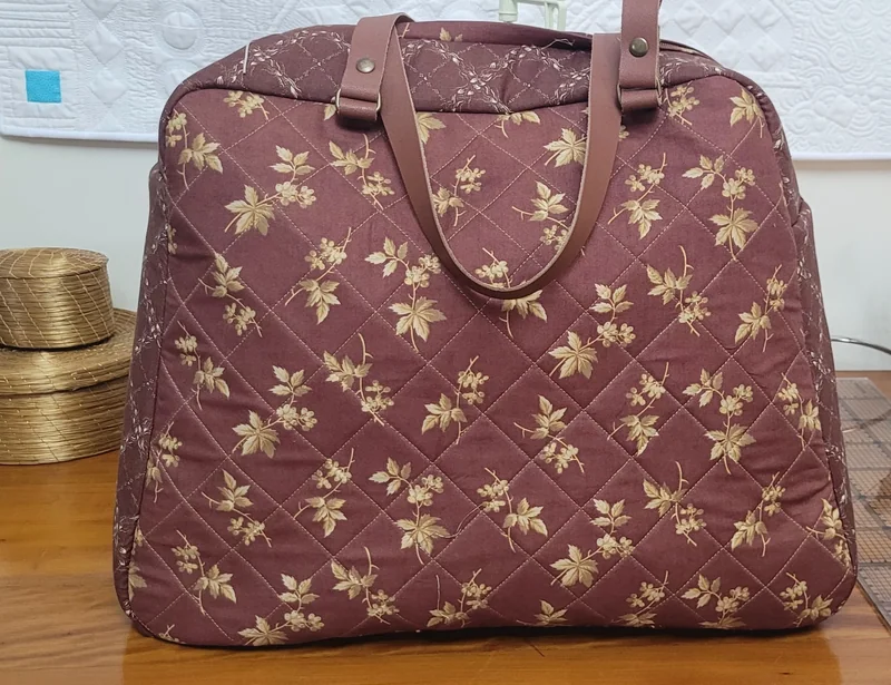 Bolsa vinho com folhas douradas, quilting em losangos e alças marrons.