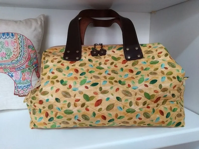 Bolsa clara com estampa de folhas e alças marrons.
