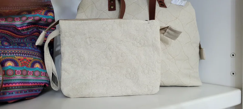 Duas bolsas de linho cru com quilting e alças marrons, ao lado de uma bolsa listrada.