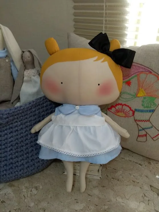 Boneca de cabelos amarelos, vestido azul-claro e laço preto na cabeça.
