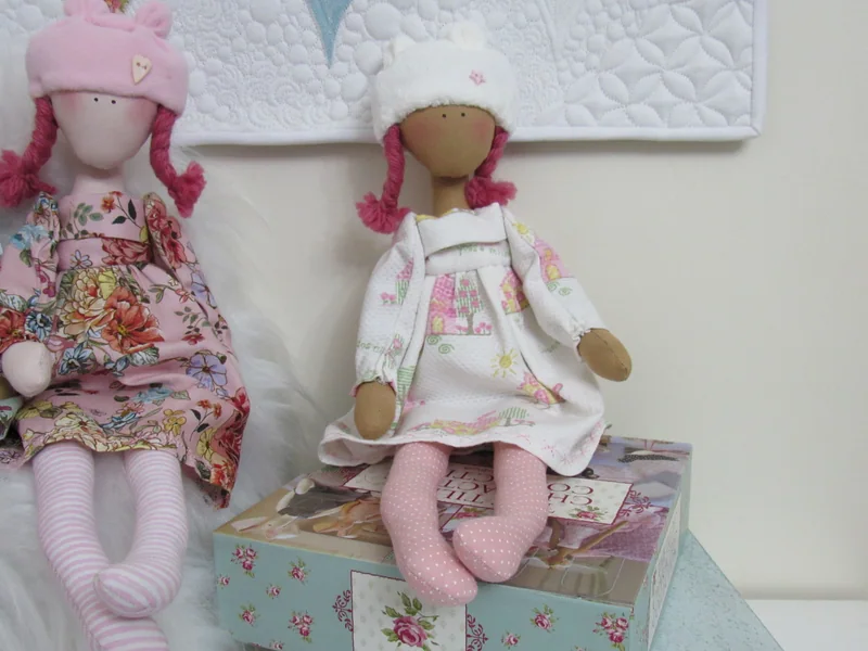 Duas bonecas de touca com vestidos estampados em tons de rosa.