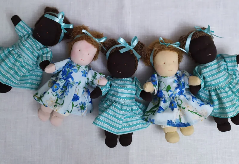 Cinco bonecas pequenas deitadas lado a lado, com vestidos azuis floridos e listrados.