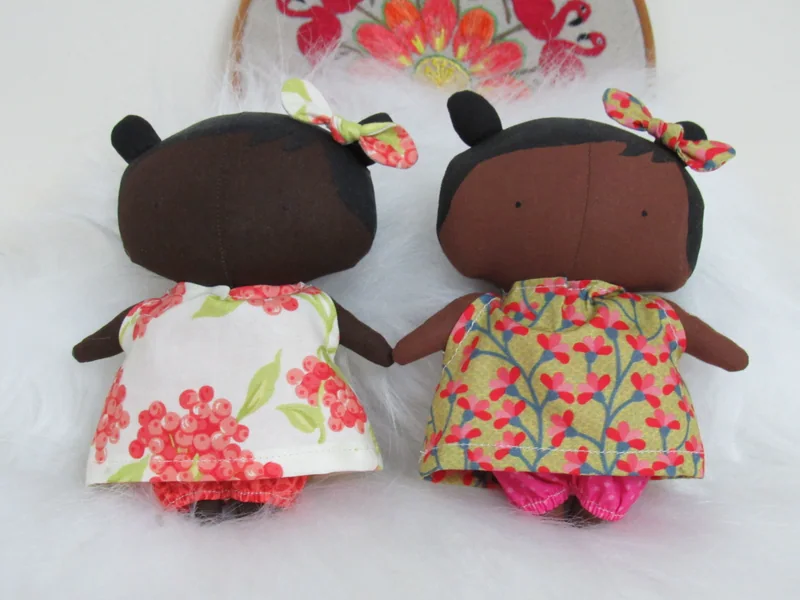 Duas bonecas de pele marrom, com vestidos florais claros.