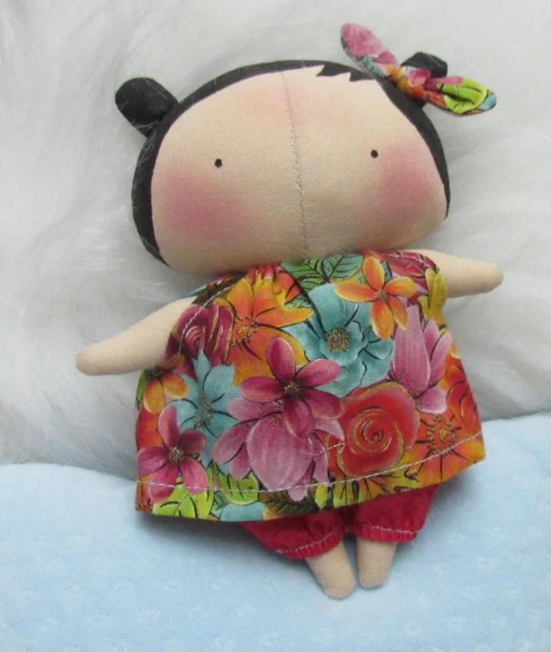 Boneca com vestido de flores coloridas e laço no cabelo.