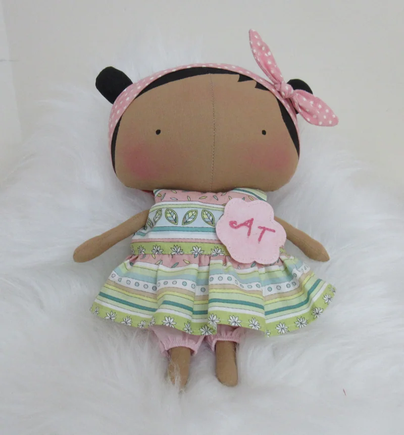 Boneca com vestido verde estampado e laço rosa no cabelo.