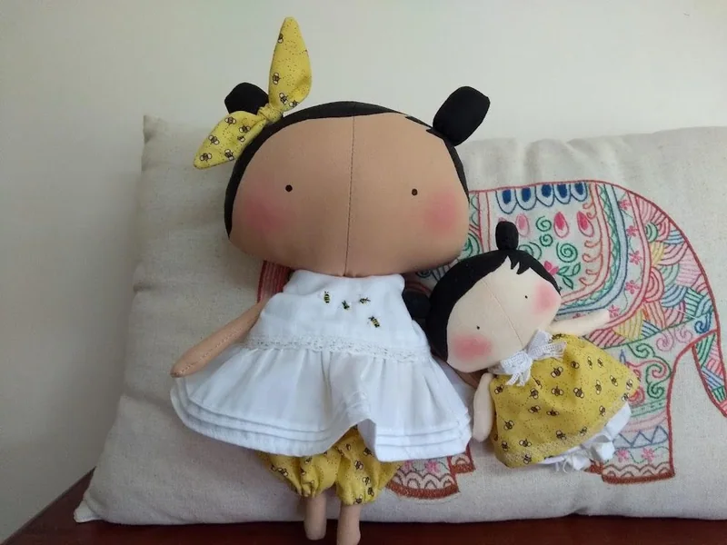 Duas bonecas de tecido com vestidos brancos, uma maior e outra menor.