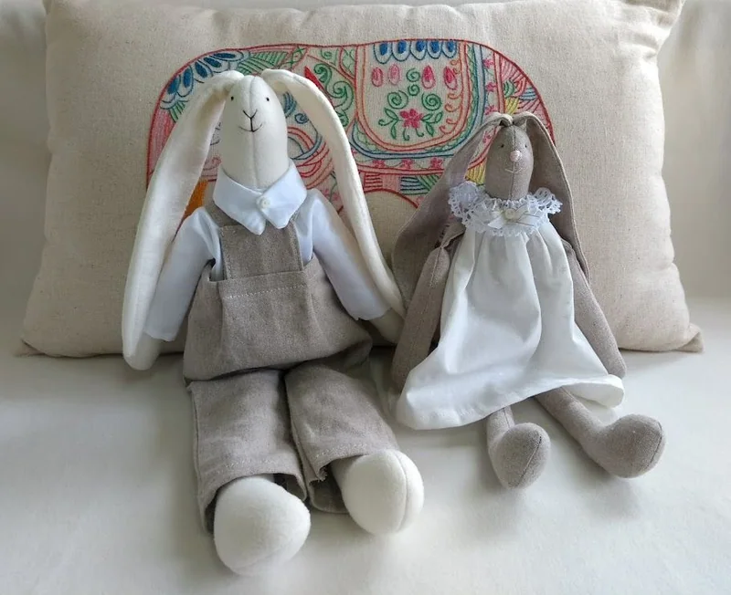 Casal de coelhos de tecido, com jardineira cinza e vestido claro.