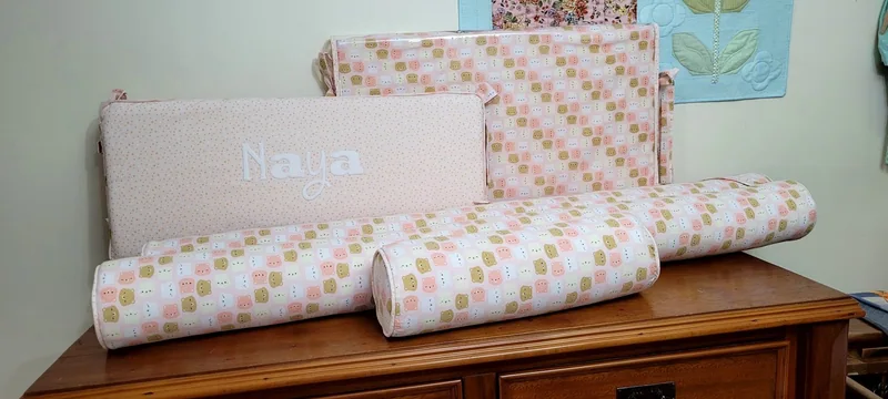 Conjunto de peças para bebê em tecido claro, com faixas e pequenos desenhos rosa e amarelos.