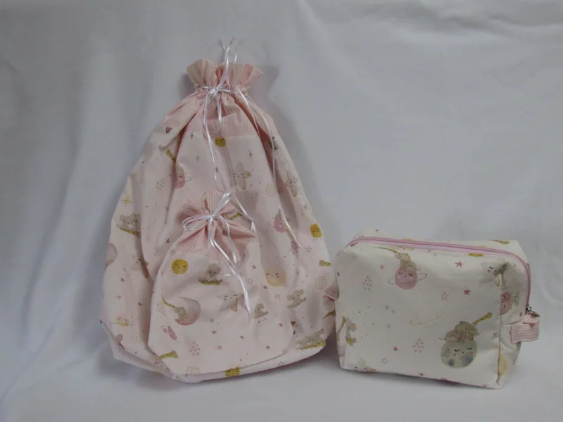 Bolsa com fechamento por cordão e nécessaire em tecidos claros com detalhes rosa.