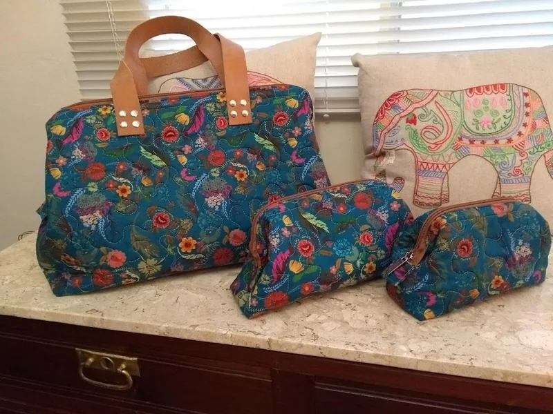 Bolsa e nécessaires florais com fundo azul e alças marrons.