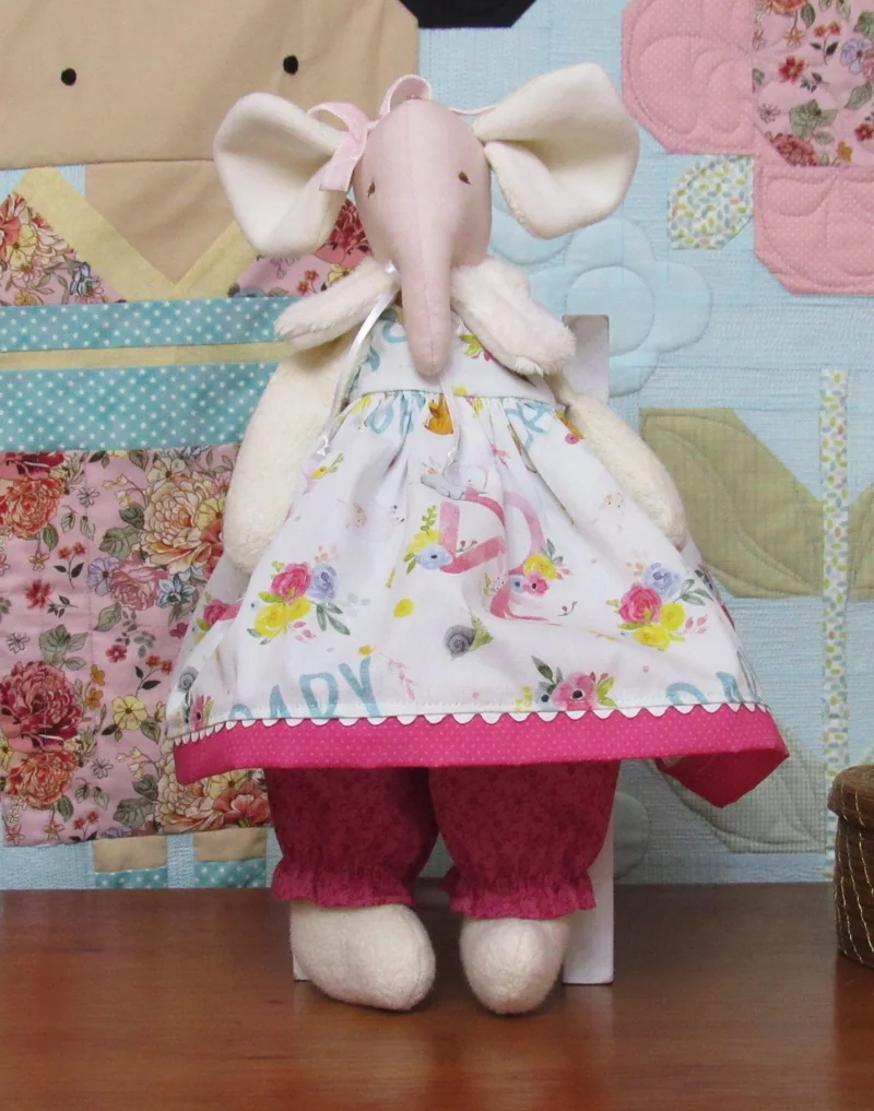 Elefantinha com vestido floral claro e barra rosa sobre calças estampadas.