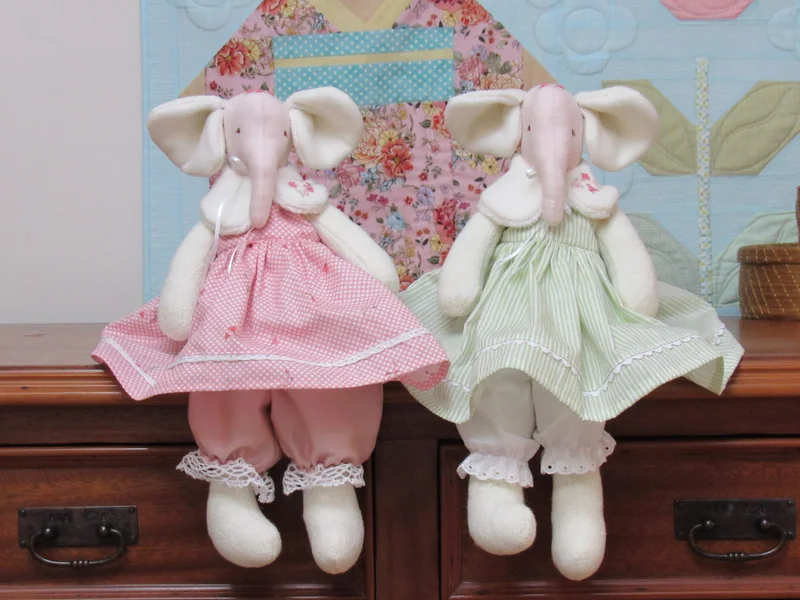 Duas elefantinhas de tecido com vestidos rosa e verde bordados.