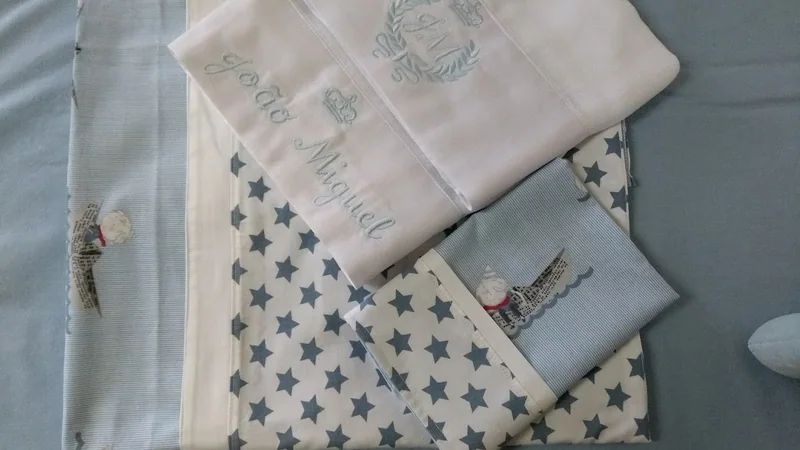 Peças de enxoval em azul-claro e branco, com estrelas e bordados.