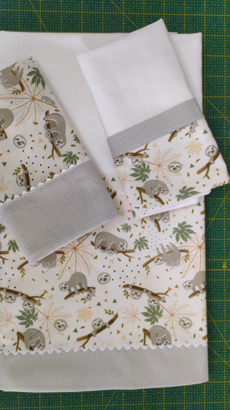 Peças de enxoval com estampa de bichos, acabamentos em verde e cinza, sobre a mesa de corte.