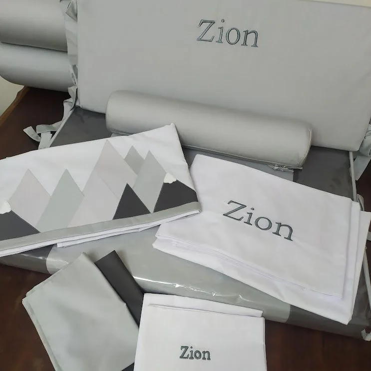 Peças de enxoval em cinza e branco, algumas com o nome Zion.