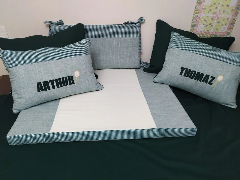 Conjunto em branco e cinza com almofadas com os nomes Arthur e Thomaz.