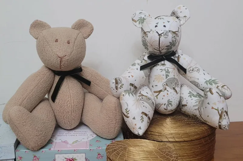 Urso bege e urso de tecido estampado, ambos com laços no pescoço.