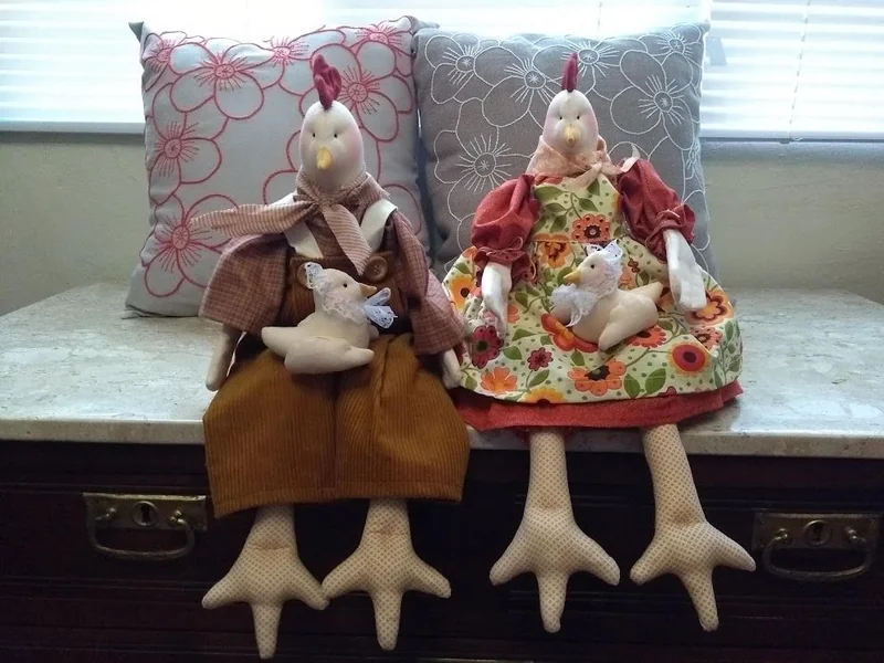 Duas galinhas de pernas compridas, vestidas e acompanhadas de pequenos pintinhos.