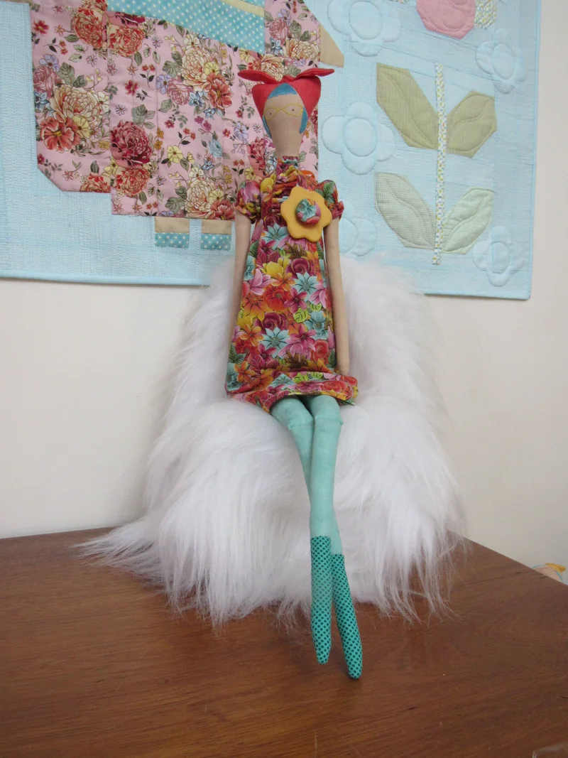 Gato de vestido floral, pernas verdes e flor amarela no peito.