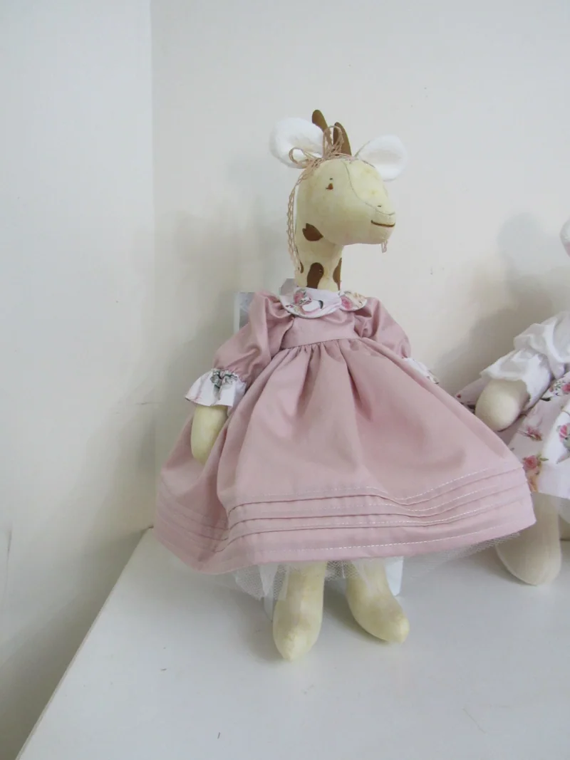 Girafa de tecido com vestido rosa e laço no pescoço.