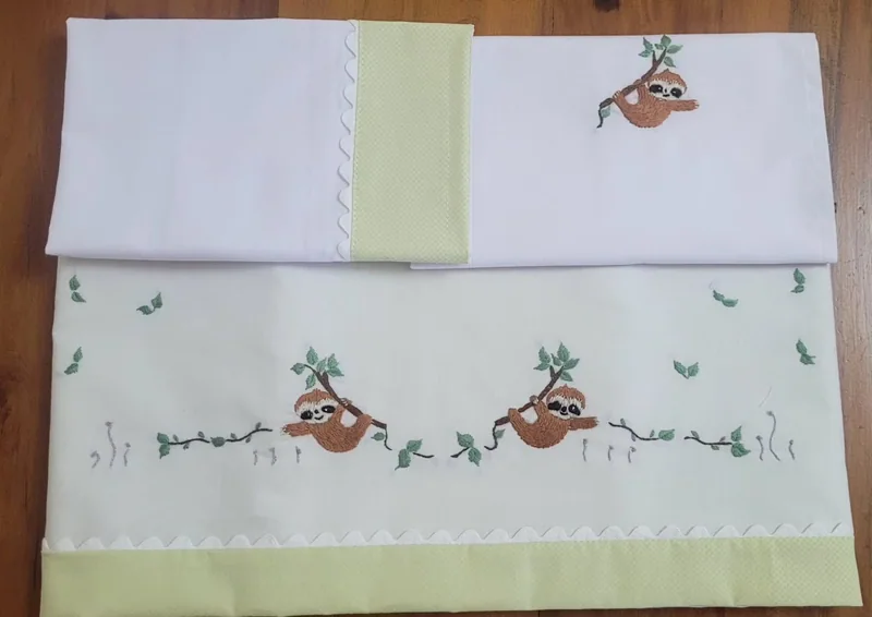 Jogo de lençol de berço branco e verde-claro com bichos bordados.