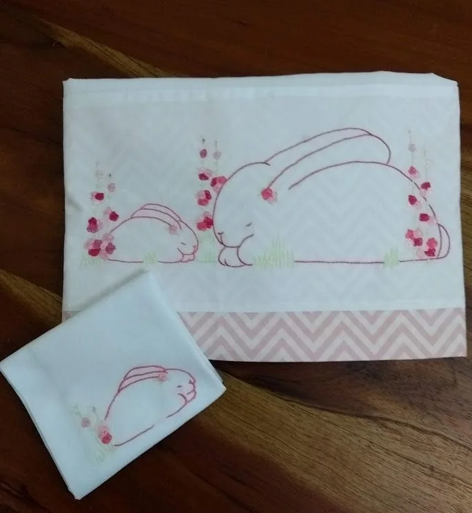 Lençol e fronha com coelho bordado em rosa e pequenas flores.