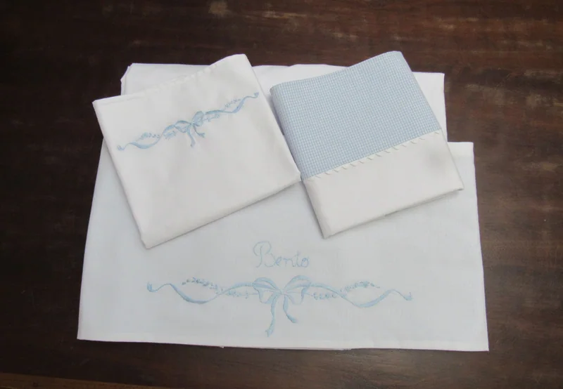 Jogo de lençol branco com acabamento azul-claro.