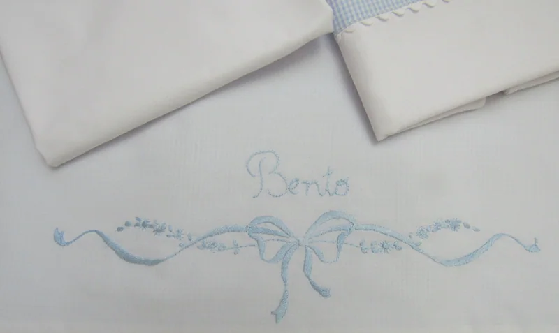 Detalhe do nome Bento e de um laço bordados em azul.