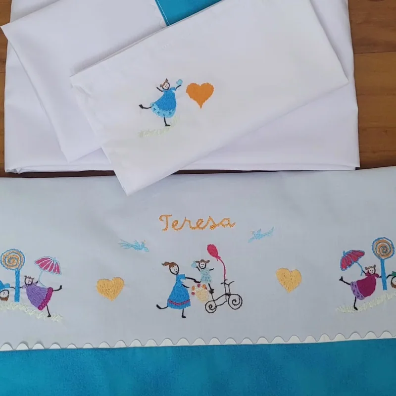 Lençol e fronha com faixa azul e personagens bordados.