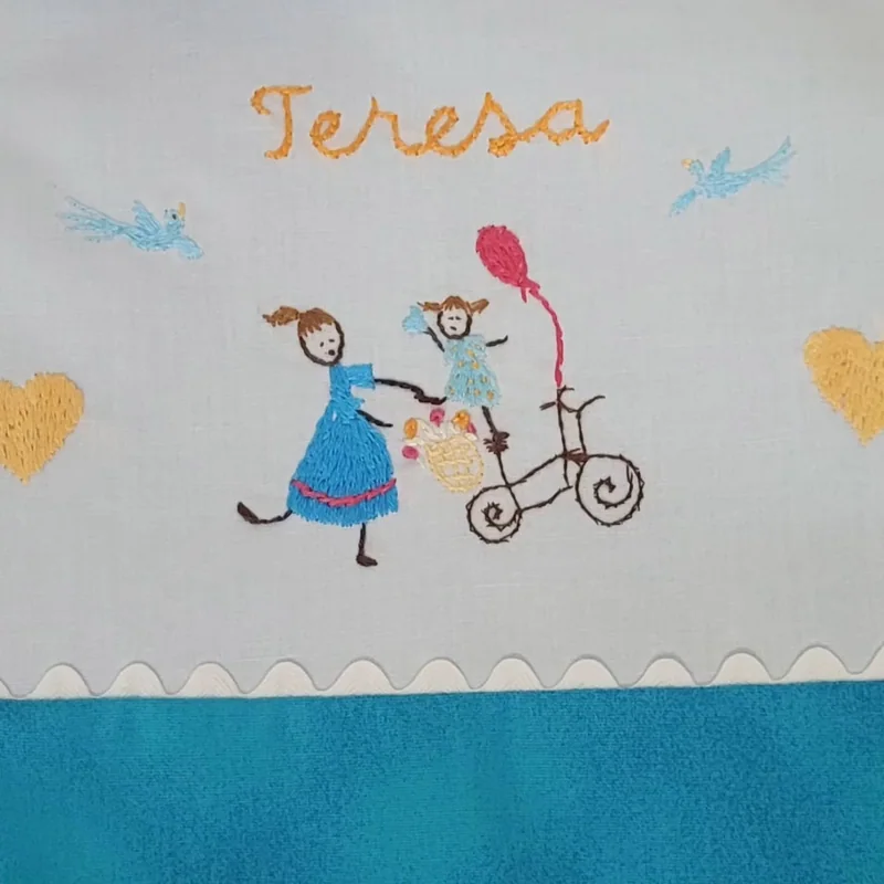 Nome Teresa e personagens bordados no tecido branco do lençol.