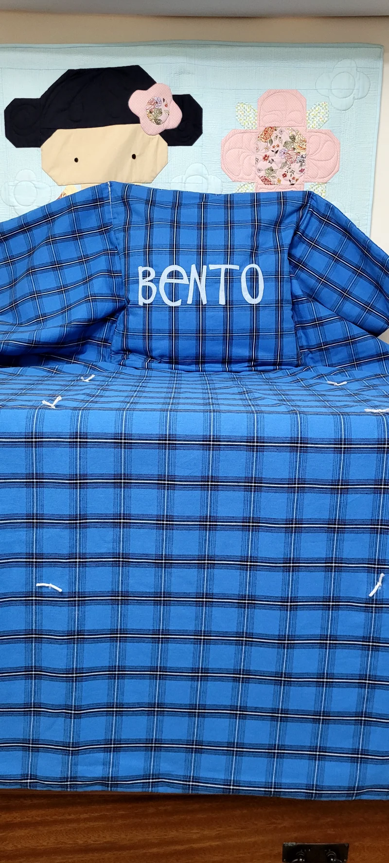Manta xadrez azul aberta sobre a cadeira, com o nome Bento bordado.