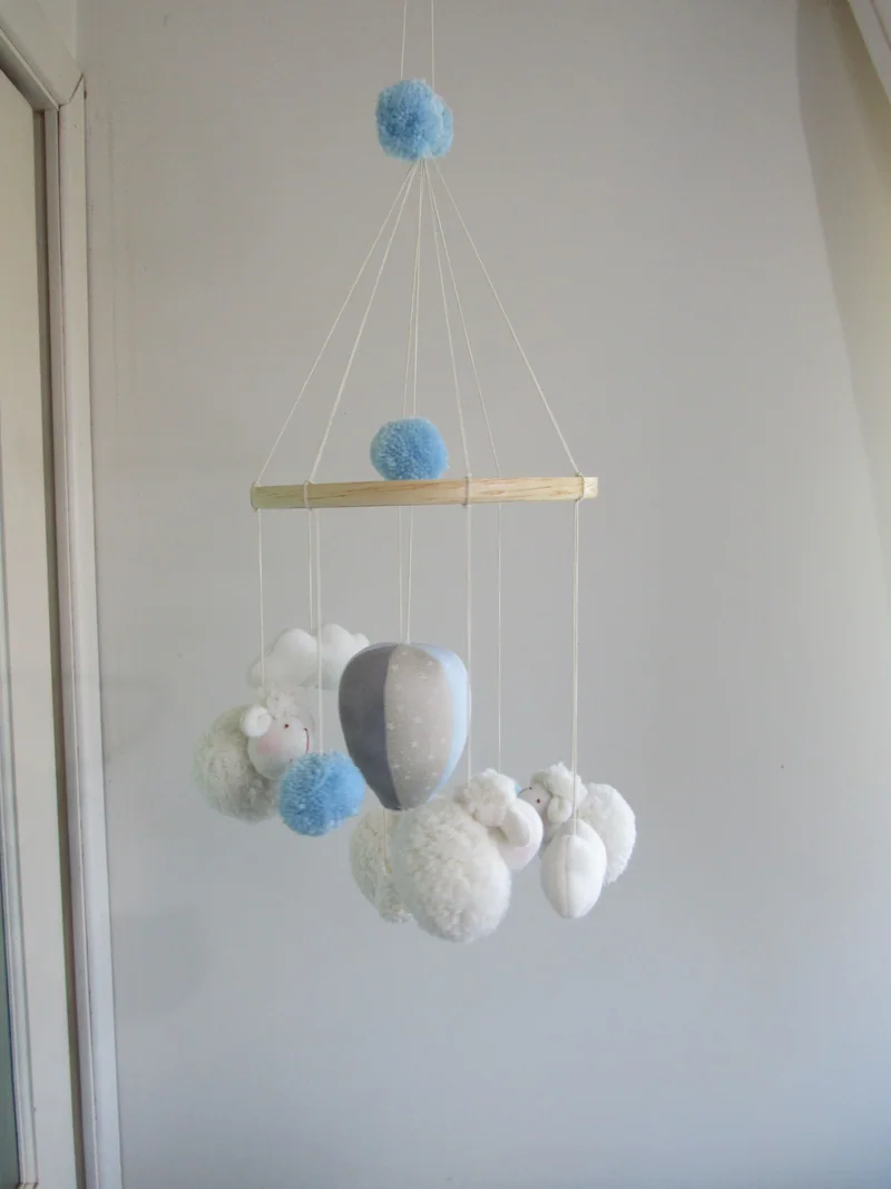 Móbile com um balão azul e cinza, nuvens brancas e esferas azuis.
