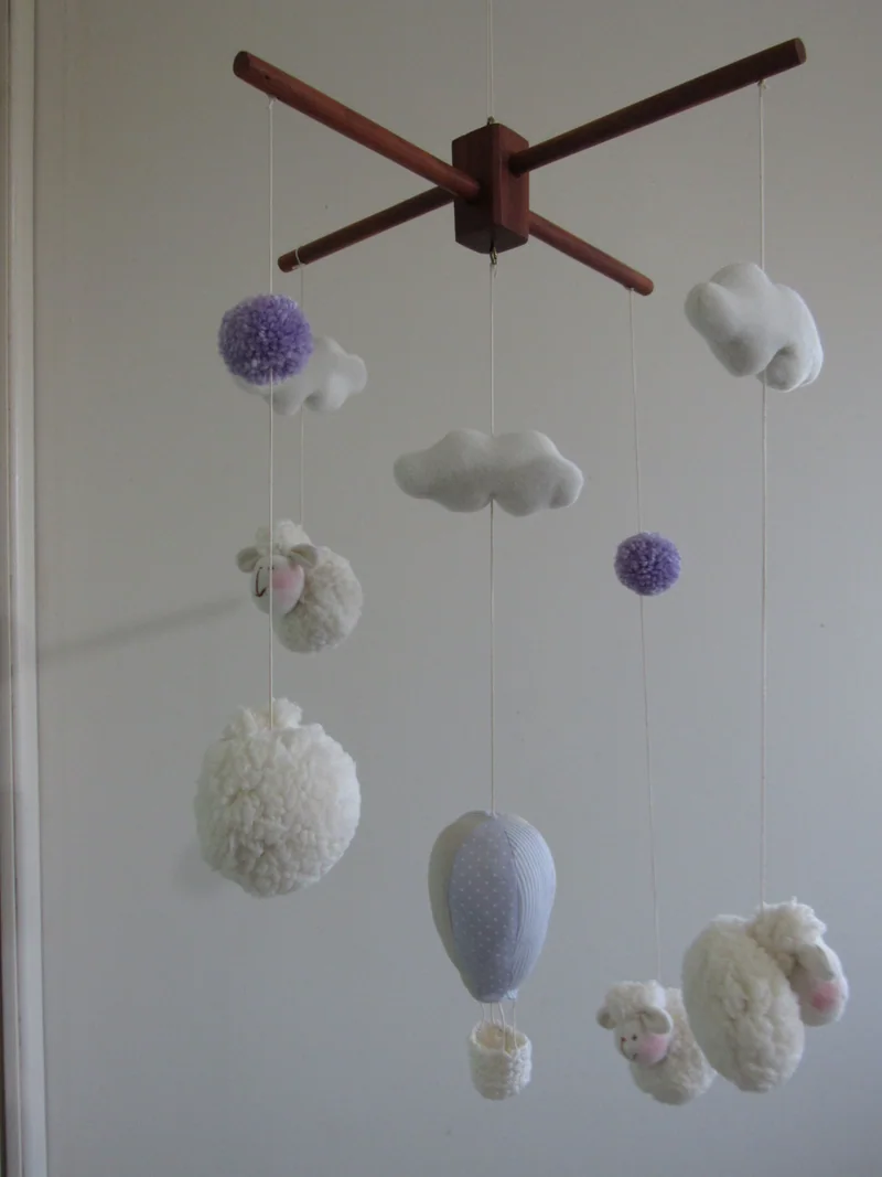 Móbile com balão lilás, ovelhinhas claras e nuvens, em suporte de madeira.