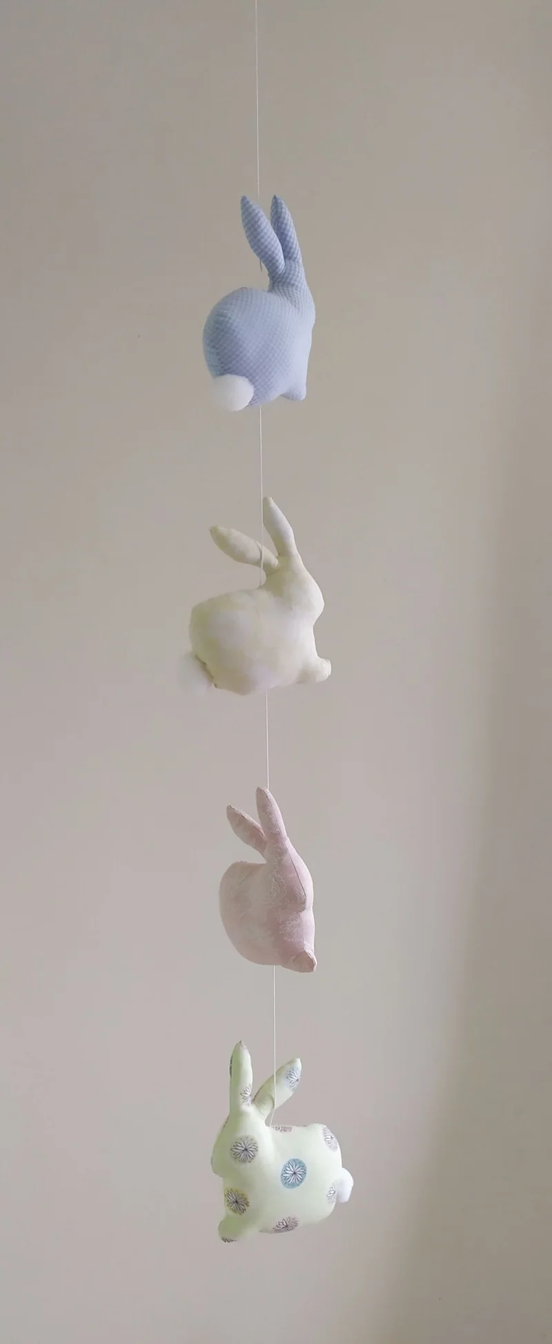 Quatro coelhinhos de tecido pendurados um abaixo do outro, em lilás, rosa, branco e florido.